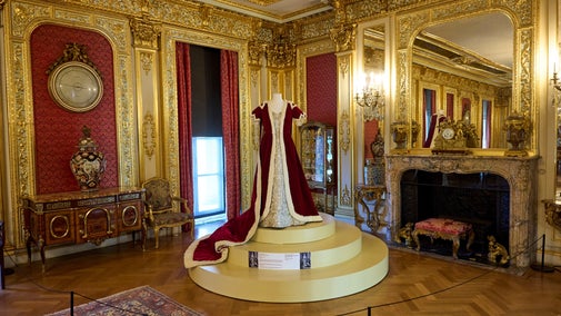A regal, red Coronation gown and robe dispalyed on a mannequin in the gold Salon at Polesden Lacey